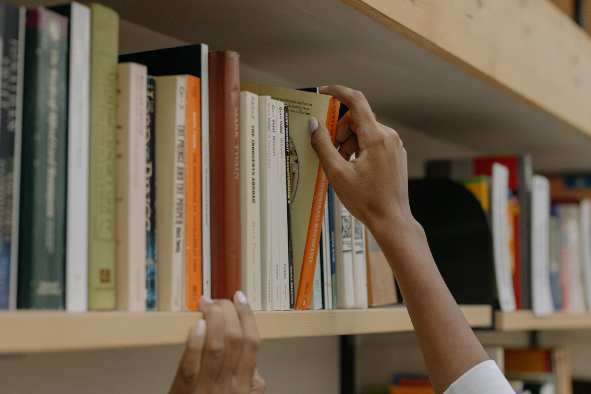 Close up on a person's hand selecting a book from a bookshelf.